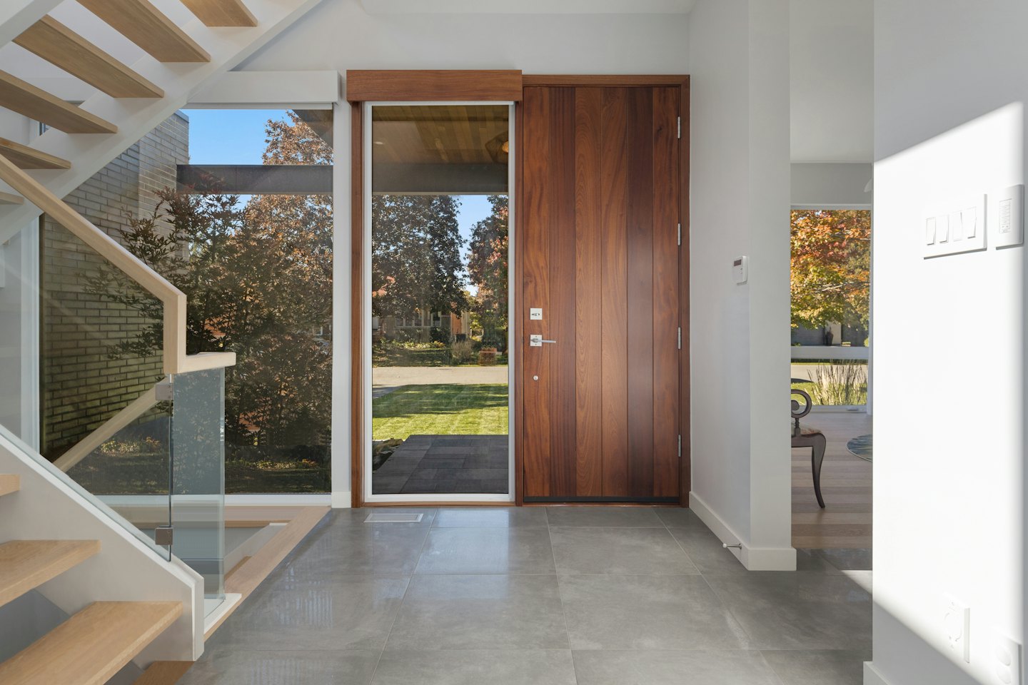 Modern entryway with wooden door and glass railed staircase.
